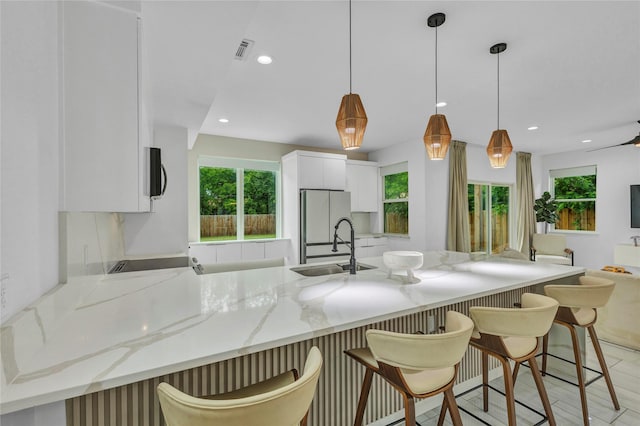1619 Homeland St, Dallas, TX 75212 - kitchen with light stone counters, freestanding refrigerator, a peninsula, white cabinetry, and visible vents