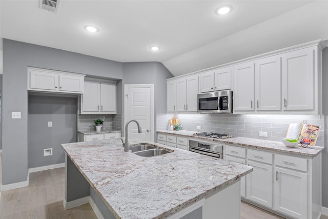 kitchen featuring appliances with stainless steel finishes, a sink, a kitchen island with sink, white cabinetry, and visible vents