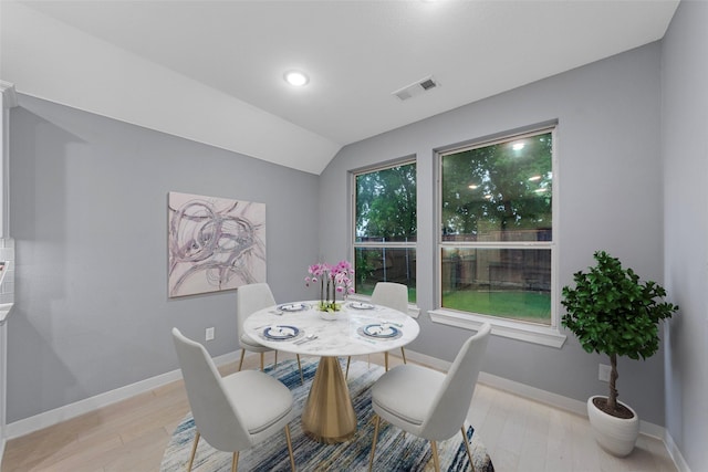 dining room with visible vents, light wood finished floors, baseboards, and vaulted ceiling