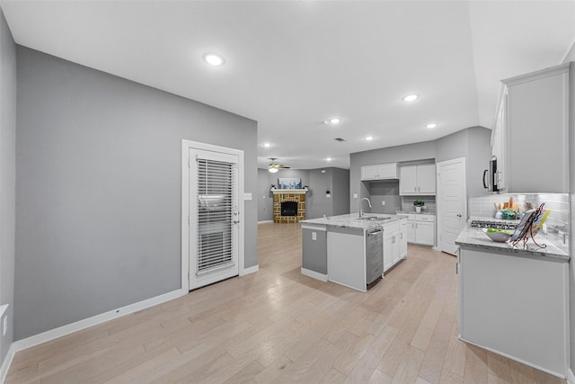 kitchen with a brick fireplace, a sink, baseboards, light stone counters, and stainless steel appliances