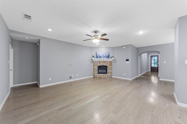 unfurnished living room featuring ceiling fan, visible vents, arched walkways, light wood-type flooring, and baseboards