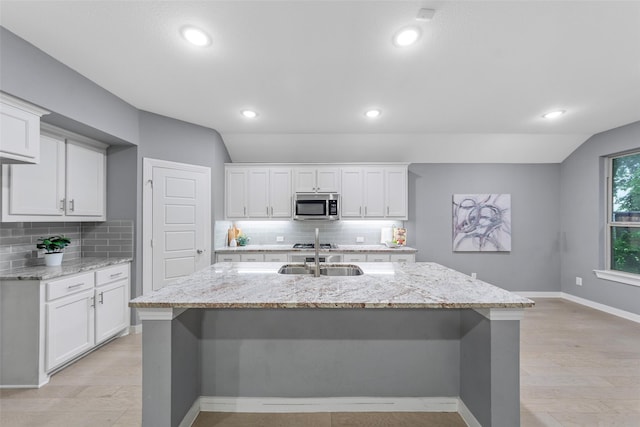 kitchen featuring white cabinets, backsplash, stainless steel microwave, and a sink