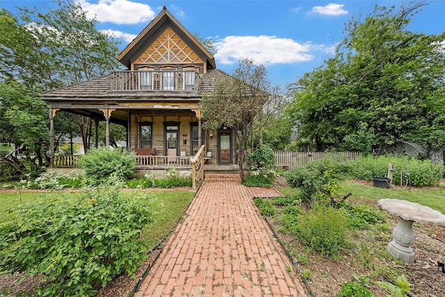 view of front of home featuring a porch, fence, and a balcony