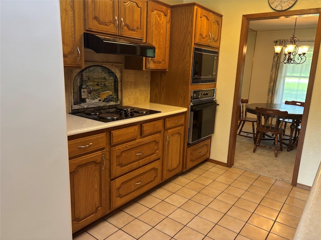 kitchen with light countertops, black appliances, a chandelier, and under cabinet range hood