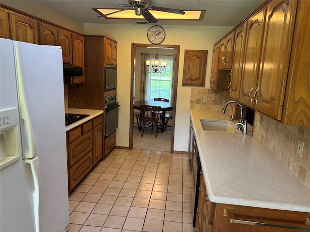 kitchen with decorative backsplash, a sink, light countertops, black appliances, and ceiling fan with notable chandelier