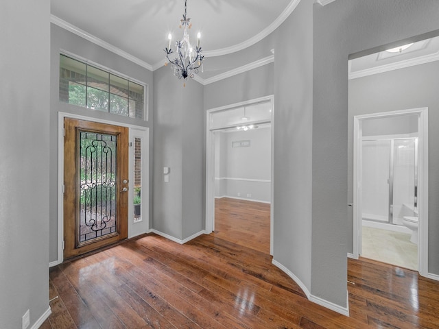 foyer entrance featuring hardwood / wood-style flooring, a high ceiling, baseboards, an inviting chandelier, and ornamental molding