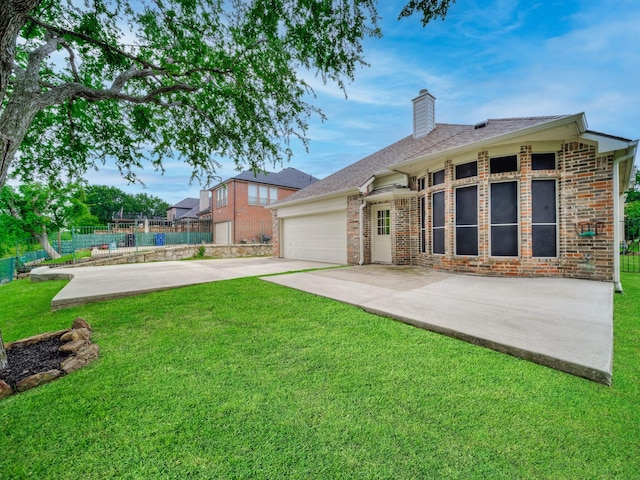 rear view of property featuring driveway, a chimney, fence, a yard, and an attached garage