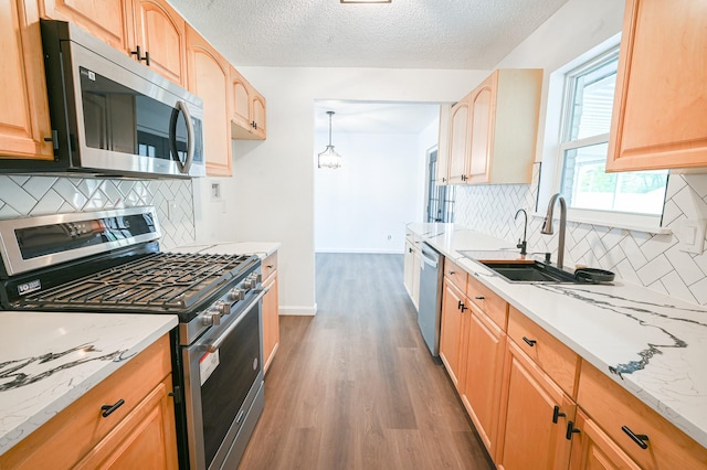 kitchen featuring light stone countertops, appliances with stainless steel finishes, a sink, decorative backsplash, and wood finished floors