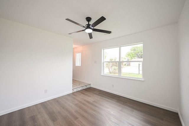 empty room with baseboards, a ceiling fan, wood finished floors, and visible vents