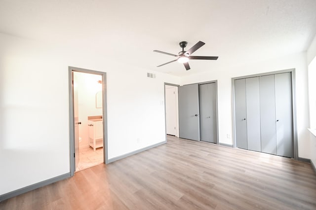 unfurnished bedroom with visible vents, baseboards, two closets, light wood finished floors, and ensuite bathroom