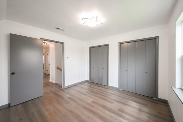 unfurnished bedroom with baseboards, two closets, wood finished floors, and visible vents