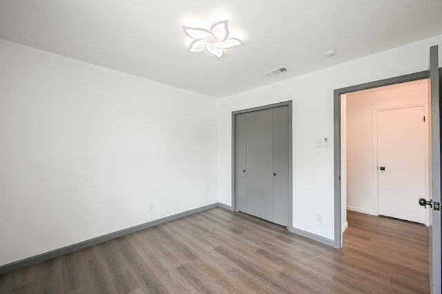 unfurnished bedroom featuring visible vents, baseboards, wood finished floors, and a closet