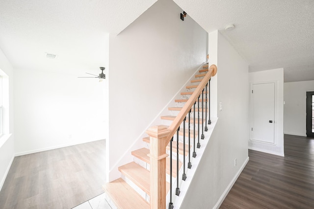 stairway with visible vents, wood finished floors, baseboards, a textured ceiling, and a ceiling fan