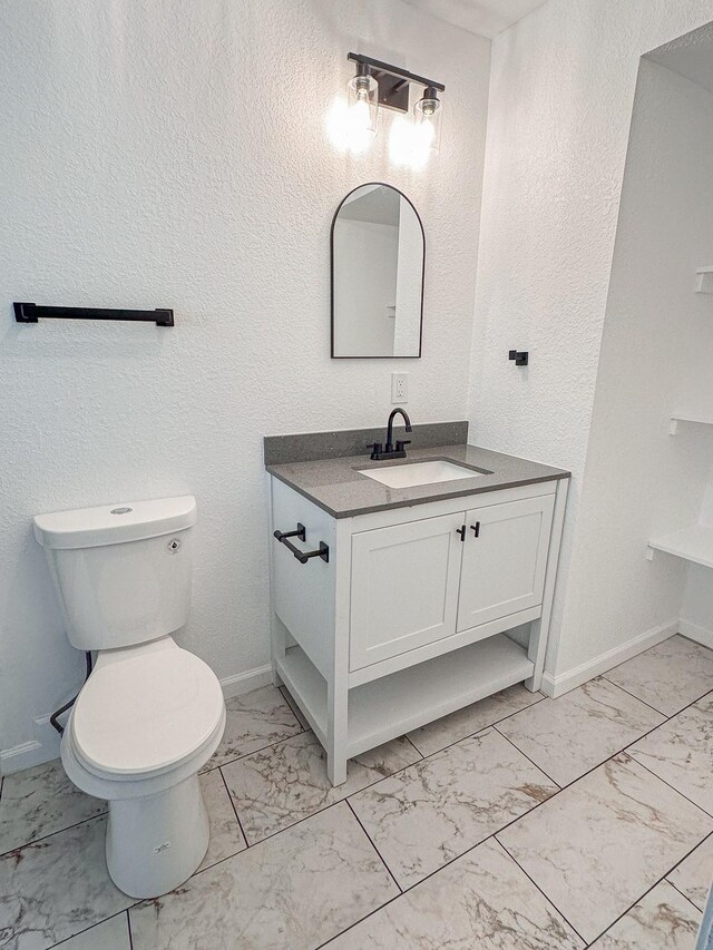 8511 Strathmore Dr, Dallas, TX 75238 - bathroom with marble look tile flooring, vanity, toilet, and baseboards