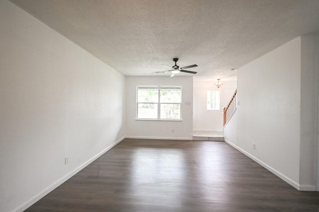 unfurnished living room with a textured ceiling, dark wood finished floors, ceiling fan with notable chandelier, baseboards, and stairway
