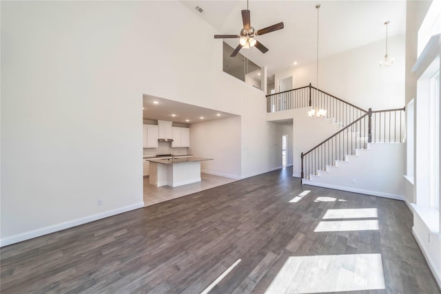341 Gleneagles Dr, Garland, TX 75040 - unfurnished living room featuring a towering ceiling, ceiling fan with notable chandelier, stairs, baseboards, and dark wood-type flooring