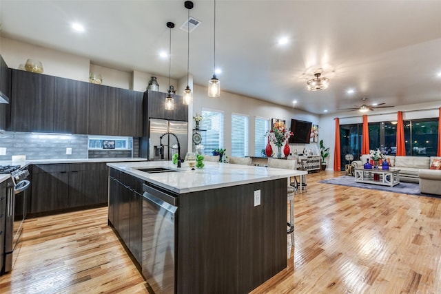11955 Hoblitzelle Dr, Dallas, TX 75243 - kitchen featuring modern cabinets, stainless steel appliances, light wood-style flooring, a center island with sink, and tasteful backsplash