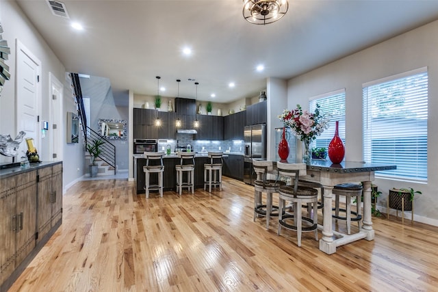 11955 Hoblitzelle Dr, Dallas, TX 75243 - kitchen with a breakfast bar, oven, light wood-type flooring, tasteful backsplash, and a kitchen island with sink
