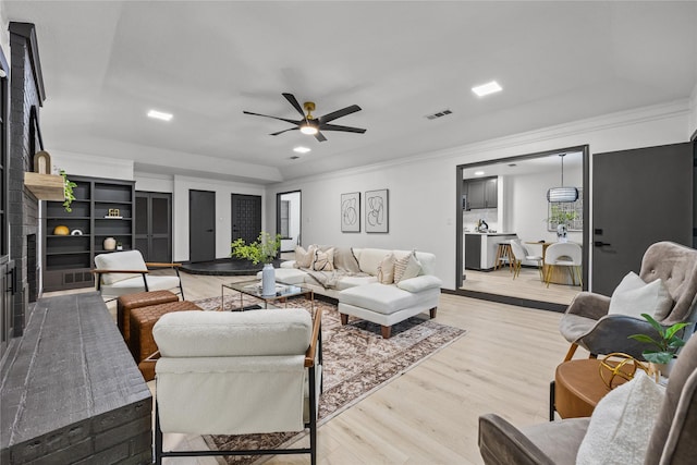 living room with light wood-style floors, ornamental molding, ceiling fan, and visible vents