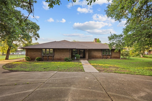 ranch-style home with a chimney, a front lawn, and brick siding
