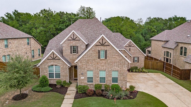 craftsman-style home with brick siding, a shingled roof, fence, and a front yard