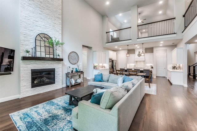 living area featuring a stone fireplace, baseboards, a high ceiling, a ceiling fan, and dark wood finished floors