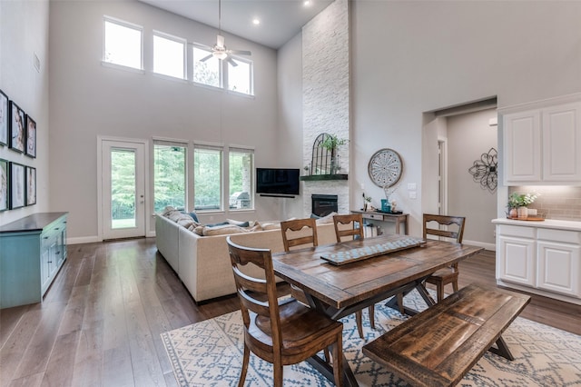 dining area featuring a high ceiling, a fireplace, wood-type flooring, and ceiling fan