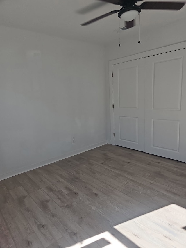 unfurnished bedroom featuring baseboards, ceiling fan, wood finished floors, and a closet