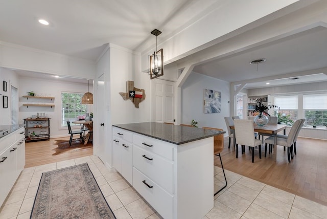 kitchen with white cabinets, crown molding, light tile patterned floors, a kitchen bar, and pendant lighting