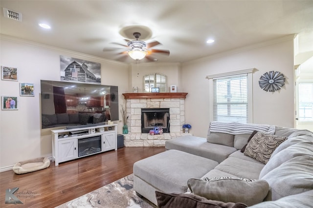 living area featuring plenty of natural light, a stone fireplace, ceiling fan, visible vents, and dark wood-type flooring