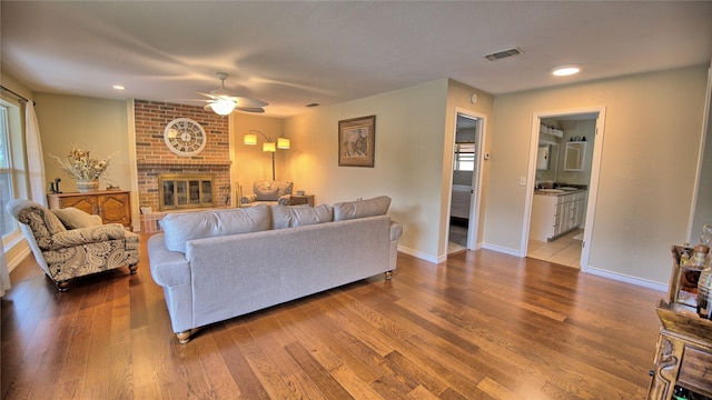 living room featuring ceiling fan, visible vents, a brick fireplace, wood finished floors, and baseboards