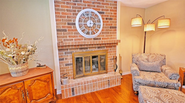 living room with a brick fireplace, baseboards, and wood finished floors