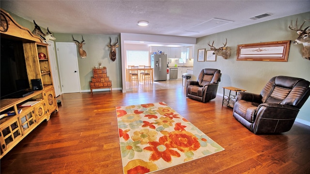 living area featuring visible vents, baseboards, a textured ceiling, and wood finished floors