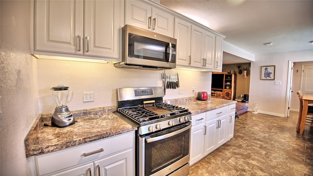 kitchen with baseboards, stone counters, appliances with stainless steel finishes, and white cabinets