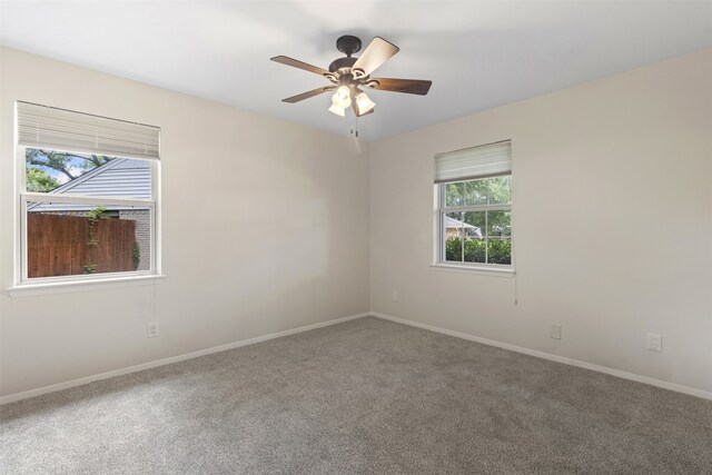 carpeted spare room featuring a healthy amount of sunlight, baseboards, and a ceiling fan