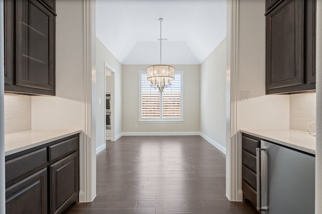 unfurnished dining area with an inviting chandelier, baseboards, dark wood-style flooring, and lofted ceiling