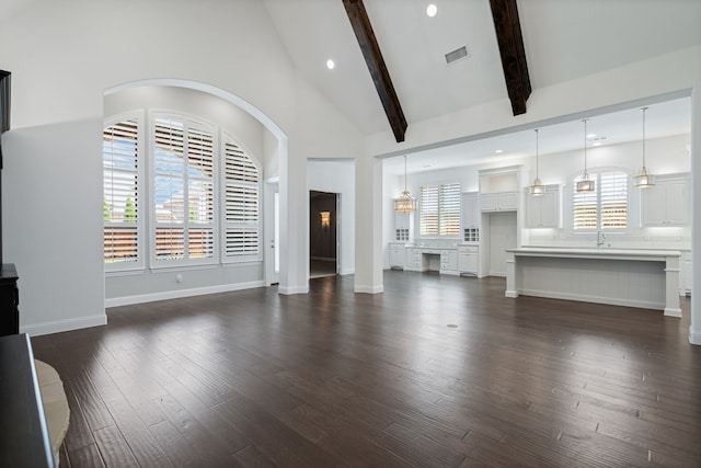 unfurnished living room with dark wood-style flooring, visible vents, plenty of natural light, and beam ceiling