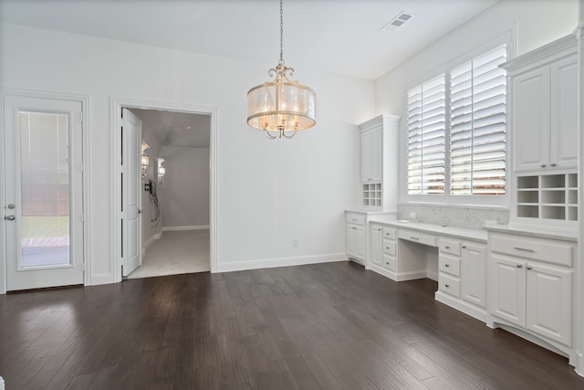 unfurnished dining area with dark wood-style flooring, a notable chandelier, built in desk, baseboards, and visible vents