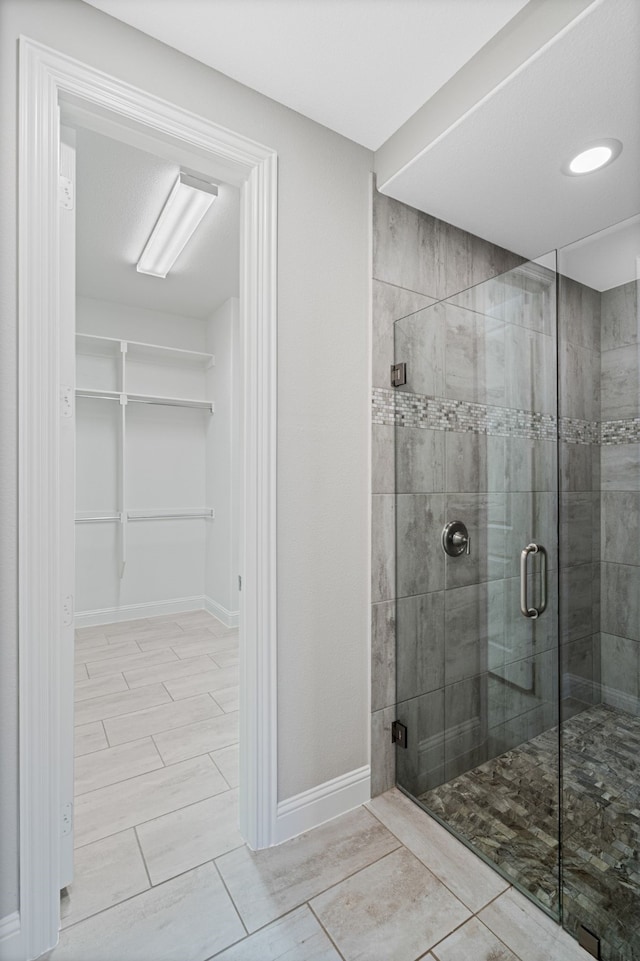 full bath featuring baseboards, a stall shower, and a spacious closet
