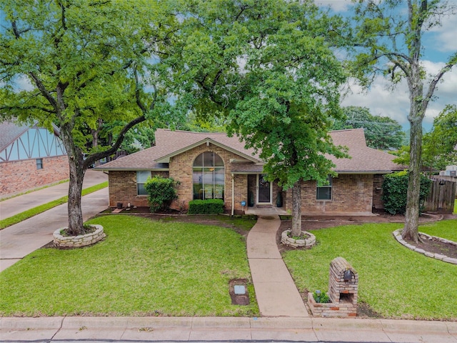 ranch-style home with a shingled roof, a front lawn, and brick siding