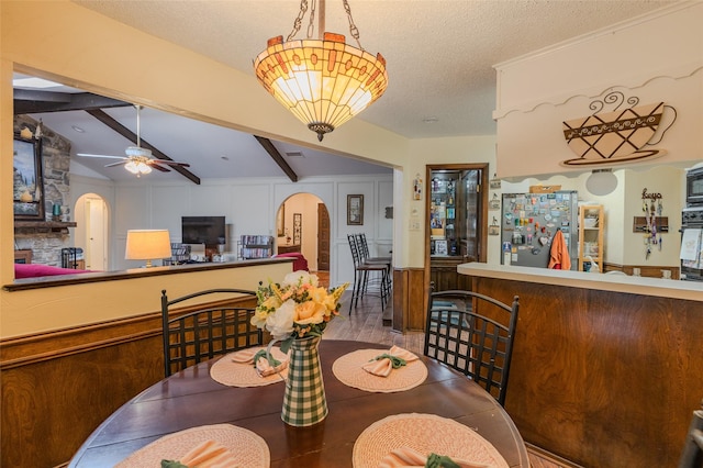 dining space featuring ceiling fan, a textured ceiling, arched walkways, a fireplace, and lofted ceiling with beams
