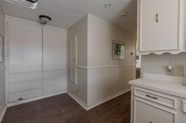 hall with a textured ceiling, baseboards, and dark wood-type flooring