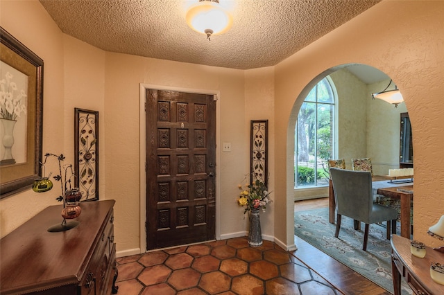 entryway with arched walkways, a textured ceiling, a textured wall, and dark tile patterned floors
