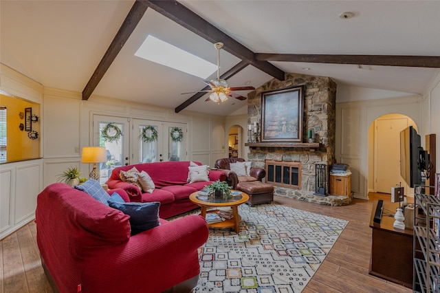living area with wood-type flooring, arched walkways, lofted ceiling with beams, and a decorative wall