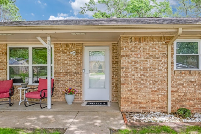 view of exterior entry with brick siding and roof with shingles
