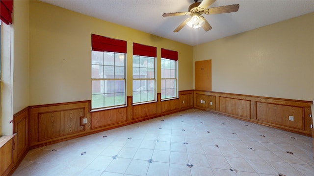 unfurnished room featuring a ceiling fan and a wainscoted wall