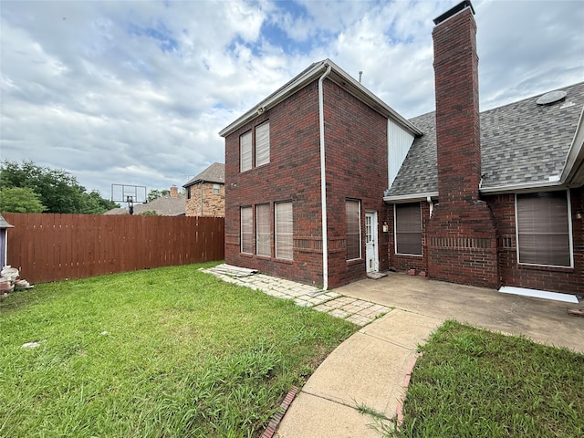 rear view of house featuring brick siding, fence, a yard, a patio, and a shingled roof