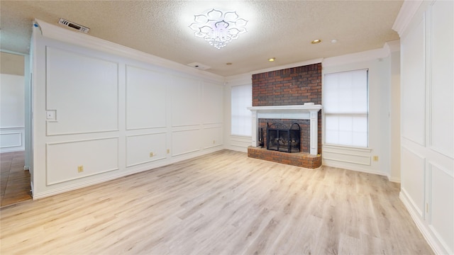 unfurnished living room featuring a textured ceiling, visible vents, a brick fireplace, light wood-style floors, and a decorative wall