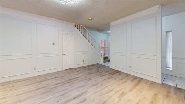 finished below grade area featuring a textured ceiling, stairs, light wood finished floors, and a decorative wall