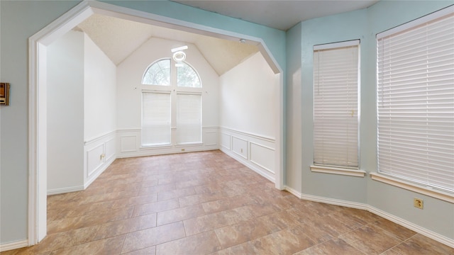 spare room featuring a decorative wall, lofted ceiling, and a wainscoted wall